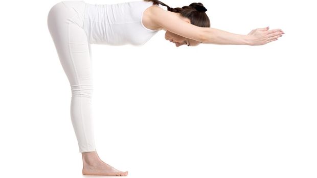 Sporty young beautiful smiling yoga female student in white sportswear doing variation of Standing Half Forward Bend, Ardha Uttanasana pose with stretched hands, studio full length shot, isolated