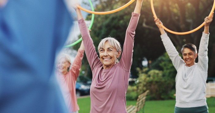 Group of seniors warming up with shoulder rolls and arm stretches in the public park.