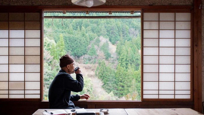 Senior Japanese artist drinking tea looking out the window. Kamikatsu, Japan.