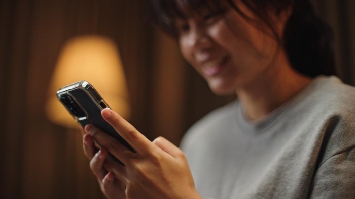 Asian young woman using smartphone on sofa at night.