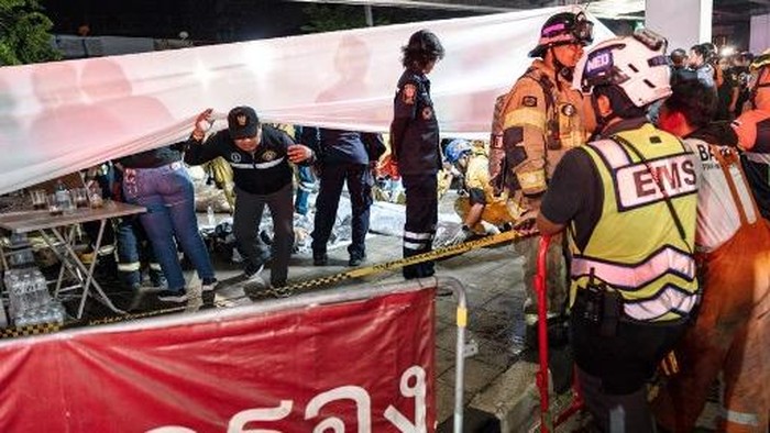 Emergency workers stand next to a white fabric displayed at the scene after a massive fire engulfed a bar in Bangkok, early on July 13, 2026. A fire in a bar in the Thai capital Bangkok killed at least 27 people late Sunday night, Prime Minister Anutin Charnvirakul told local media. (Photo by chanakarn LAOSARAKHAM / AFP)