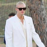 Jas itu dipadukan dengan kemeja putih berkerah terbuka tanpa dasi, sehingga memberi kesan formal namun tetap santai. Rambut pirang panjang penyerang Norwegia itu disisir rapi ke belakang (slicked back), sementara kacamata hitam berbingkai tebal dan bros rantai berwarna perak yang menghiasi kerah jas menjadi aksen yang memperkuat tampilannya. (Foto: Vittorio Zunino Celotto/GC Images)