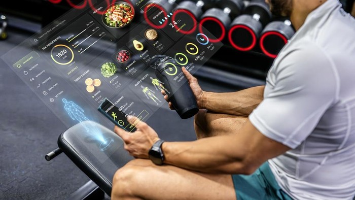 Fit man holding smart phone and shaker while monitoring healthy eating, hydration, and fitness goals