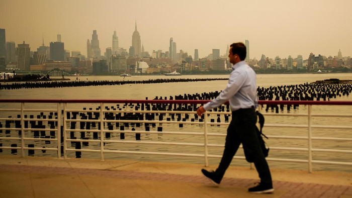 A man walks while The New York City skyline and the Empire State Building are seen through a cover of wildfire smoke as seen from Newport, New Jersey, U.S., July 16, 2026. REUTERS/Eduardo Munoz