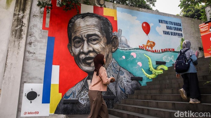 Pengunjung melintas di depan mural bertema 100 tahun kelahiran Ali Sadikin di Taman Ismail Marzuki, Jakarta, Jumat (17/7/2026). Karya tersebut menjadi penghormatan atas kontribusinya dalam pembangunan Jakarta.