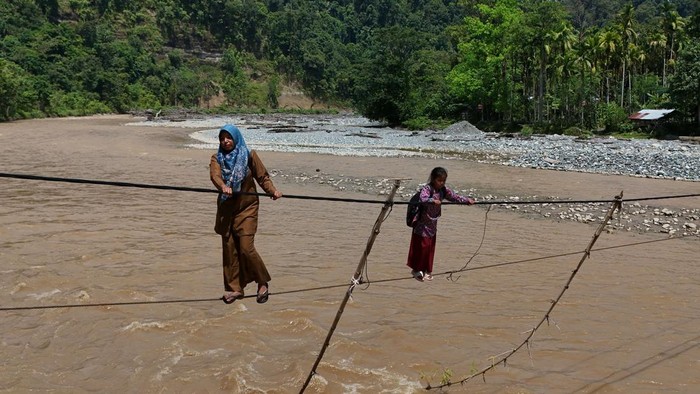 Guru dan siswa melintasi jembatan tali baja penghubung Dusun Sarah Sare dan Dusun Durian saat pulang sekolah di Desa Sikundo, Kecamatan Pante Ceureumen, Aceh Barat, Aceh, Senin (20/7/2026). Guru dan siswa di kawasan itu terpaksa menggunakan jembatan tali baja untuk berangkat dan pulang sekolah pasca rusaknya jembatan gantung penghubung antar dusun pada akhir November 2025 lalu. ANTARA FOTO/Syifa Yulinnas/nz.