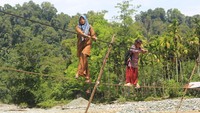 Guru dan siswa melintasi jembatan tali baja saat pulang sekolah di Desa Sikundo, Kecamatan Pante Ceureumen, Aceh Barat, Aceh. Jembatan tersebut menjadi akses utama setelah jembatan gantung penghubung antar dusun rusak. Foto: ANTARA FOTO/SYIFA YULINNAS