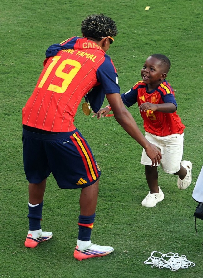 Mengenakan jersey  Timnas Spanyol bernomor punggung 19 milik Lamine Yamal dengan nama Keyne di bagian belakang, ia langsung berlari ke arah sang kakak. Yamal pun menyambutnya dengan pelukan hangat sebelum mengangkat Keyne ke udara dan memakaikan topi merah bertuliskan Lamine di kepalanya. (Foto: REUTERS/John Sibley)