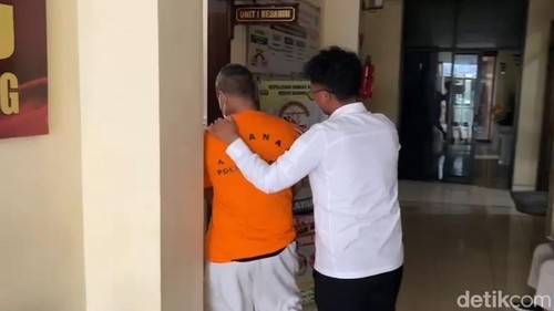 Tersangka HSH, memakai baju tahanan digiring ke ruang penyidik Satreskrim Polres Badung sebelum dirilis polisi, Senin (20/7/2026). (Agus Eka)