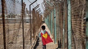 Karya Fahad Aloudah. Di jalan setapak sempit di antara pagar kawat berduri di kamp pengungsi Zaatari di Yordania utara, seorang anak Suriah (lahir di kamp tersebut) dengan riang berlarian sambil mengenakan jubah Superman merah yang berkibar di belakangnya. Kain jubah yang cerah kontras dengan lingkungan yang keras dan berpagar, mengubah pengasingan yang keras menjadi ruang imajinasi. Jubah merah itu lebih dari sekadar kain; itu adalah simbol bahwa bahkan dalam keadaan tersulit sekalipun, pahlawan super dapat lahir. Foto: HIPA