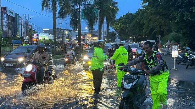 Polantas Polda Riau turun membantu pengendara di tengah jalanan banjir di Kota Pekanbaru, Senin (20/7/2026).