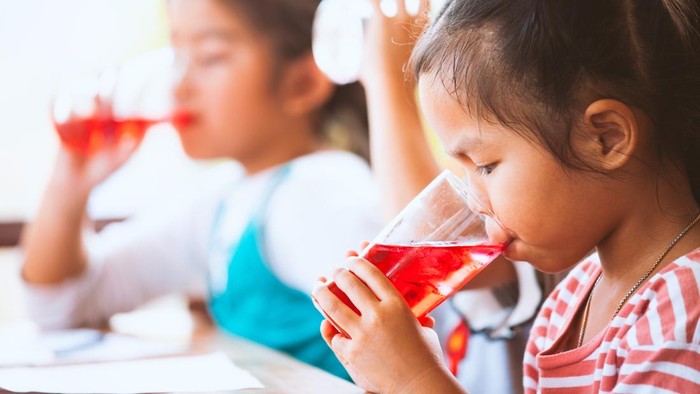 Group of asian children drinking red juice water with ice from glass together in the summer time