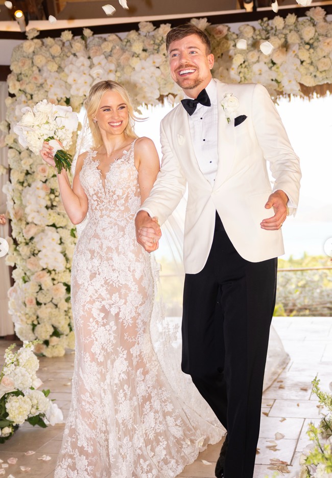 Thea terlihat anggun dengan gaun pengantin bersiluet fit-and-flare atau mendekati mermaid, yang mengikuti lekuk tubuh hingga pinggul lalu melebar ke bagian bawah. Gaun tersebut didominasi kain lace (renda) bermotif yang tampak sedikit menerawang pada bagian bawahnya. Foto: Instagram/@mrbeast