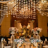 Dekorasi pernikahan Ayu dan Ruwadi tampak sangat megah dan elegan dengan langit-langit yang dihiasi bunga ronce melati dan lilin-lilin kristal yang mewah. Area akad nikah ditata dengan estetis menggunakan meja cermin yang memantulkan keindahan dekorasi, serta kursi beraksen emas dengan hiasan bunga bernuansa lembut. Foto: Dok. Instagram @ayupratiwi.