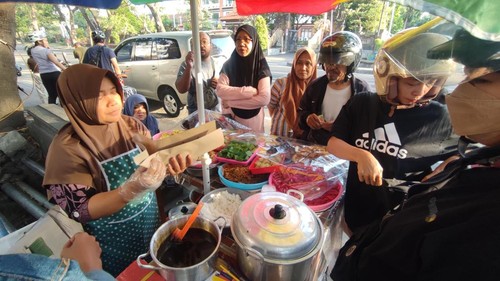 Nur Hayati (45), penjual jajanan Bali khas Karangasem, melayani pembeli di lapak jualannya, Jalan Raya Puputan, Denpasar, Sabtu (25/7/2026). (Ahmad Firizqi Irwan/detikBali)