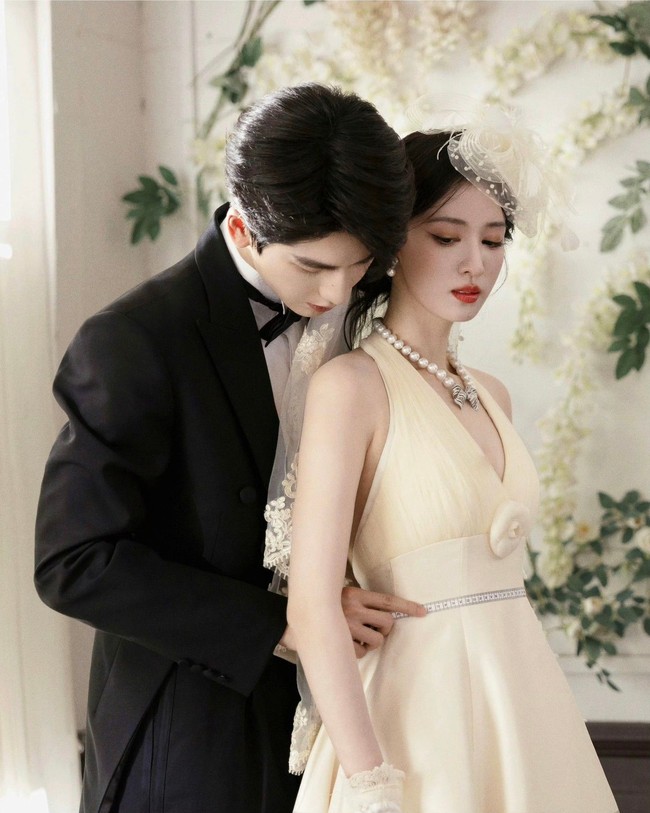 Salah satu foto memperlihatkan Wang Churan yang tampil anggun mengenakan gaun pengantin putih saat menjalani adegan fitting busana. Di belakangnya, Zhang Linghe berdiri sambil membantu proses persiapan, menciptakan suasana yang terasa hangat dan penuh perhatian. Foto: Dok. Weibo