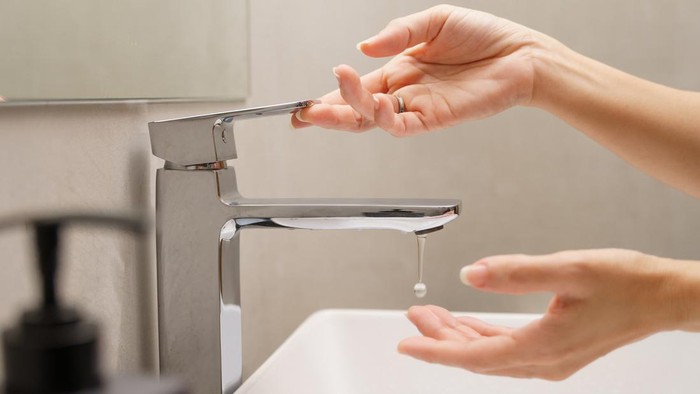 Close up of womans hand turn on faucet and a drop of water dripping out into hand at white ceramic wash basin in modern design bathroom