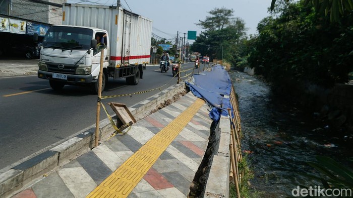 Seorang pejalan kaki beraktivitas di Jalan Raya Sawangan, Rabu (29/7/2026). Trotoar yang baru berusia satu tahun itu nampak amblas dan rusak.