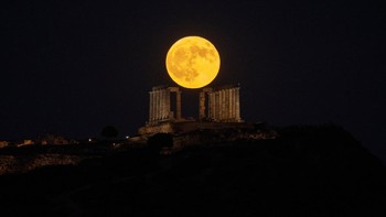 Bulan purnama yang dikenal sebagai Buck Moon terlihat muncul di balik Kuil Poseidon kuno di Cape Sounion, selatan Athena, Yunani, Rabu (29/7/2026). Fenomena bulan purnama tersebut menjadi salah satu momen astronomi yang menarik perhatian warga dan fotografer di berbagai belahan dunia. REUTERS/Louiza Vradi  