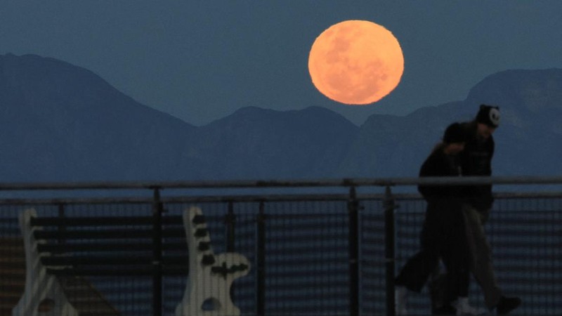 People walking on the promenade as the full moon rises over Muizenberg, in Cape Town, South Africa, July 29, 2026. REUTERS/Esa Alexander