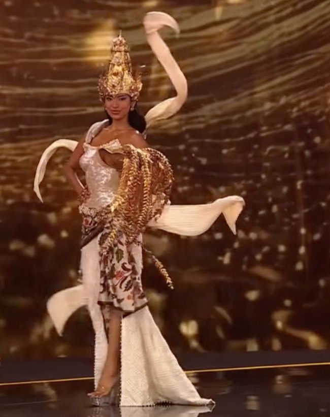 Gaun rancangan desainer Dibba ini menghadirkan siluet menyerupai kemben modern berwarna putih mutiara dengan efek berkilau, dipadukan kain batik bermotif flora yang menjuntai hingga lantai. Foto: Instagram/@misssupranational