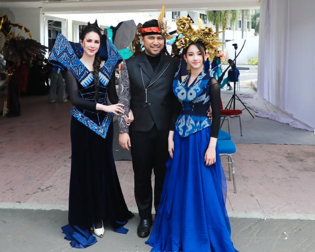 Sementara Lakeisha mengenakan gaun panjang berwarna biru elektrik dengan rok flowy yang jatuh ringan hingga lantai. Bagian atas busana dihiasi panel bermotif tenun biru, hitam, dan putih yang senada dengan sang mama. Penampilannya semakin mencuri perhatian berkat hiasan kepala berukuran besar berwarna emas berbentuk rangkaian bunga dan daun. Foto: Instagram/@arumibachsin_94