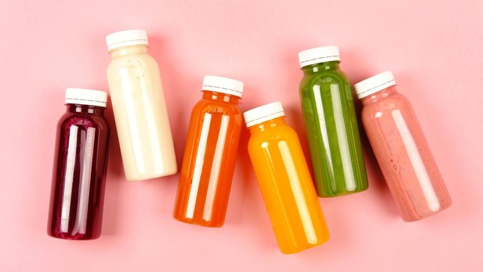 Bottles of multicolored smoothies or juices on pink background. Flat lay style.