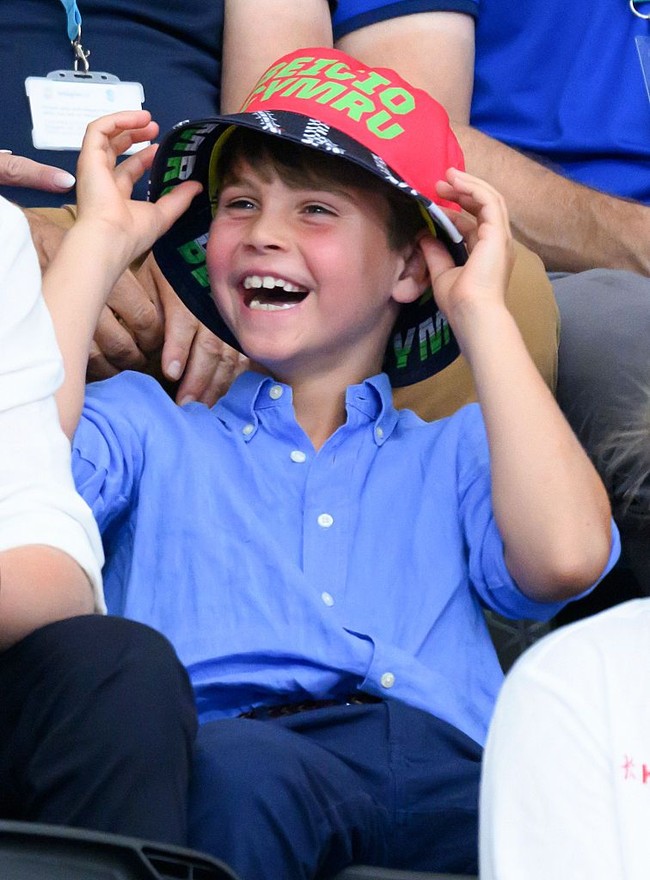 Louis tampaknya tak bisa menolak kesempatan untuk mencoba topi bucket berwarna merah bertuliskan bahasa Wales Beicio Cymru” atau Welsh Cycling. Ia bahkan menarik topi tersebut hingga menutupi matanya sebelum tertawa lepas. Tingkahnya sontak membuat orang-orang di sekitarnya ikut tersenyum. (Foto: Karwai Tang/WireImage)