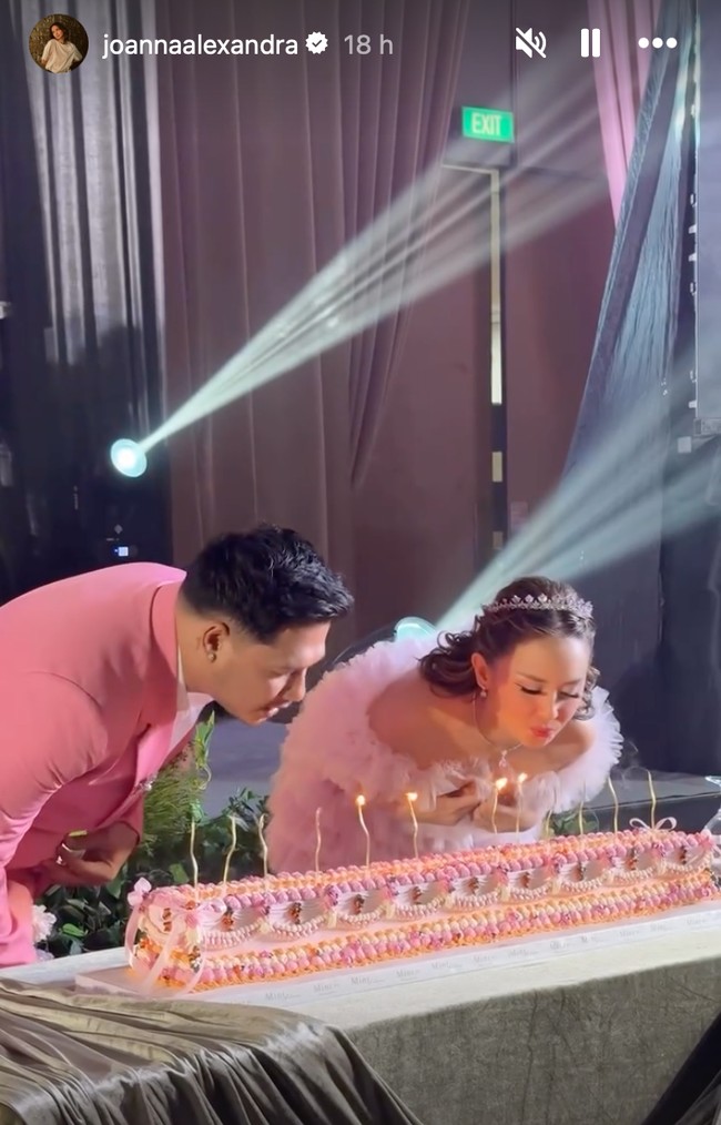 Senada dengan busana kedua mempelai, kue pernikahan dibuat memanjang dengan dominasi warna pink. Di bagian atasnya terdapat lilin-lilin yang dinyalakan untuk ditiup oleh Joanna dan Chris. Foto: Instagram/@joannaalexandra