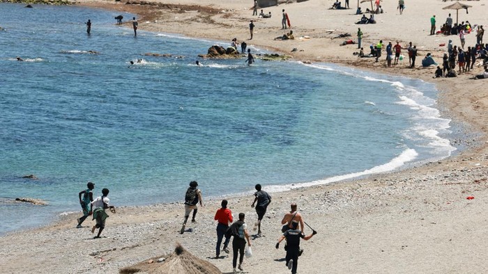 A Spanish police officer prevents migrants leaving from the perimetered area of the beach guarded by police, in Ceuta, Spain, following deadly mass crossings of migrants on foot and by sea from Morocco into Spanish territory, August 2, 2026. REUTERS/Violeta Santos Moura