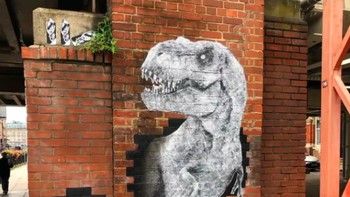 Mr T-Rex karya Shaun Hodgkin di Portsmouth, Inggris, membuat dinosaurus raksasa tampak menerobos dinding jembatan dekat Stasiun Portsmouth & Southsea. Mural stencil ini menjadi bagian dari festival LOOK UP Portsmouth 2025. Foto: via StreetArtUtopia