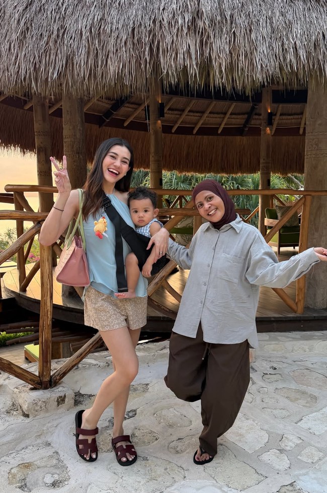 Aaliyah tampil santai padukan busana halter neck biru muda dengan celana pendek motif floral. Ia juga terlihat tetap memilih untuk momong putranya sendiri. Foto: Instagram/@thariqhalilintar