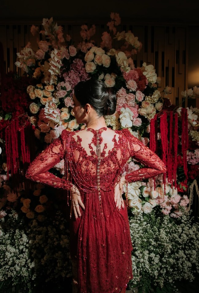 Dari foto belakang terlihat salah satu daya tarik utama kebaya tersebut, yaitu desain open-back illusion yang dihiasi bordiran simetris. Bagian tengah punggung dilengkapi deretan kancing kecil memanjang sebagai detail dekoratif, sementara terdapat untaian manik-manik yang menjuntai dari bahu hingga punggung sehingga menciptakan efek dramatis saat dikenakan. Foto: Instagram/@deaaannisa