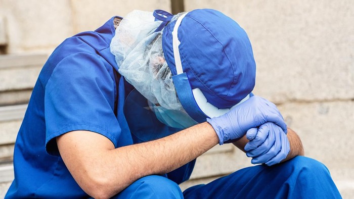 Young serious overworked, male mature health care worker sitting looking down very sad