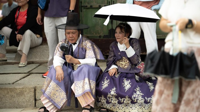 SEOUL, SOUTH KOREA - AUGUST 05: Tourists clad in traditional Korean hanbok attire use hand fans and umbrellas to shelter themselves from the summer heat as they stroll through the grounds of Gyeongbokgung Palace in Seoul, South Korea, on August 05, 2026. (Photo by Hwawon Lee/Anadolu via Getty Images)
