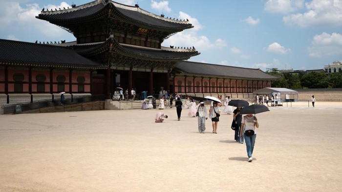SEOUL, SOUTH KOREA - AUGUST 05: Tourists clad in traditional Korean hanbok attire use hand fans and umbrellas to shelter themselves from the summer heat as they stroll through the grounds of Gyeongbokgung Palace in Seoul, South Korea, on August 05, 2026. (Photo by Hwawon Lee/Anadolu via Getty Images)