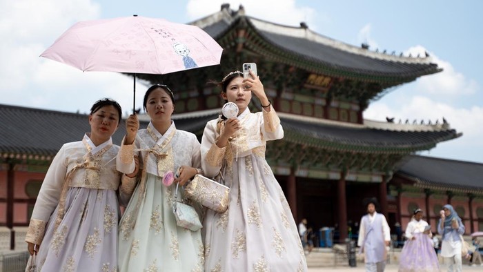 SEOUL, SOUTH KOREA - AUGUST 05: Tourists clad in traditional Korean hanbok attire use hand fans and umbrellas to shelter themselves from the summer heat as they stroll through the grounds of Gyeongbokgung Palace in Seoul, South Korea, on August 05, 2026. (Photo by Hwawon Lee/Anadolu via Getty Images)