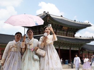 SEOUL, SOUTH KOREA - AUGUST 05: Tourists clad in traditional Korean hanbok attire use hand fans and umbrellas to shelter themselves from the summer heat as they stroll through the grounds of Gyeongbokgung Palace in Seoul, South Korea, on August 05, 2
