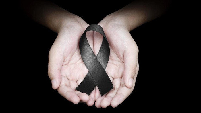 Hand holding black ribbon on black background mourning awareness sign