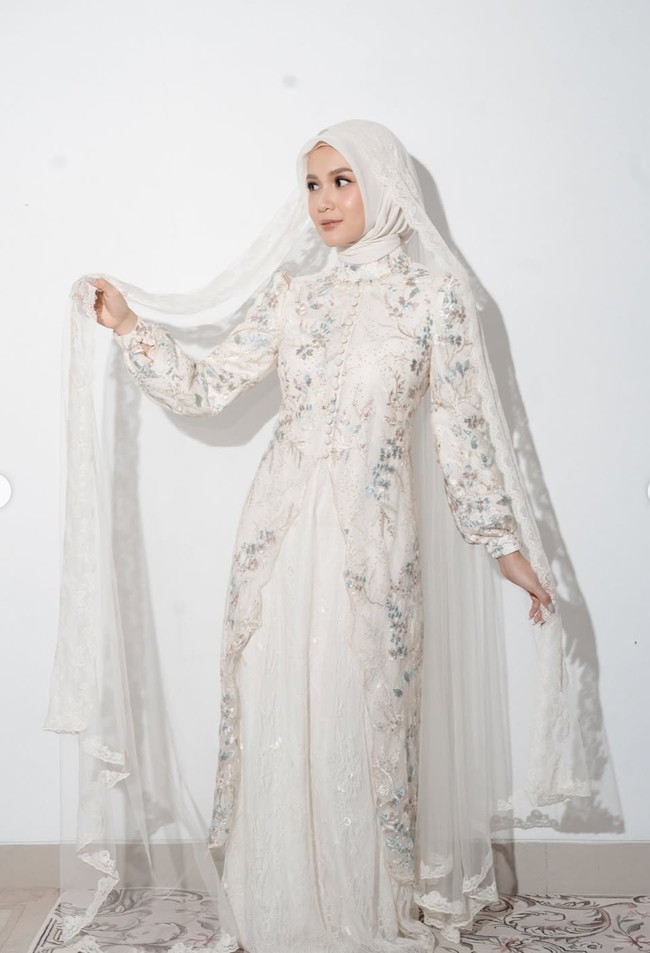 Bagian depan gamis dihiasi detail bordir serta ornamen floral yang memberikan kesan mewah. Siluet busana tampak mengikuti bentuk tubuh di bagian atas, kemudian jatuh panjang hingga menyentuh lantai. Foto: Instagram/@deaaannisa