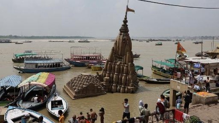 People walk past a Hindu temple partially submerged in floodwaters, along the banks of river Ganges in Varanasi on August 8, 2026. (Photo by Niharika KULKARNI / AFP)
