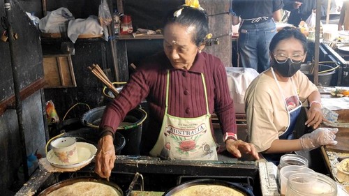 Ni Mangku Renggani tengah menyajikan terang bulan jadul untuk pelanggan saat berjualan di Pasar Beringkit, Desa Mengwitani, Kecamatan Mengwi, Badung, Minggu (9/8/2026) sore. (Agus Eka/detikBali)