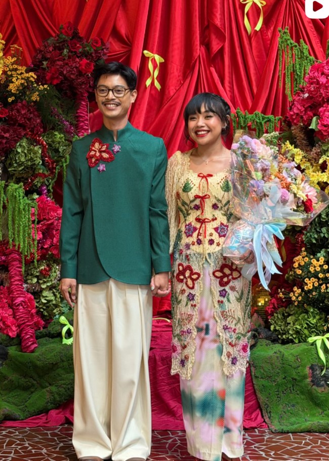 Di acara lamaran, Aulion dan Pila tampil dengan busana perpaduan tradisional dan kontemporer. Pila mengenakan busana dengan dasar warna pastel transparan, didominasi perpaduan pink, hijau, biru, dan warna lembut lainnya. Bagian luarnya berupa kebaya panjang bernuansa krem dihiasi aplikasi bunga warna-warni. Foto: Instagram/@pnvl