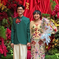 Di acara lamaran, Aulion dan Pila tampil dengan busana perpaduan tradisional dan kontemporer. Pila mengenakan busana dengan dasar warna pastel transparan, didominasi perpaduan pink, hijau, biru, dan warna lembut lainnya. Bagian luarnya berupa kebaya panjang bernuansa krem dihiasi aplikasi bunga warna-warni. Foto: Instagram/@pnvl
