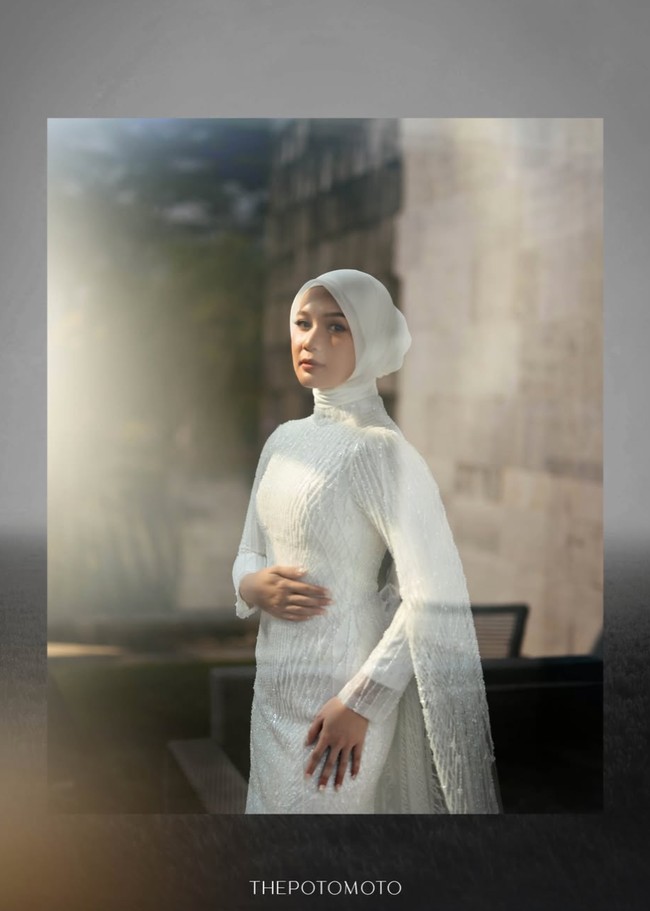Gaun pengantin putih berlengan panjang itu memiliki siluet yang mengikuti bentuk tubuh. Gaun tersebut tampak simpel dan elegan dengan dipenuhi payet senada. Bagian lengannya dilengkapi kain menjuntai seperti cape yang jatuh sampai ke bawah, menciptakan kesan dramatis. Foto: Instagram/@deaaannisa