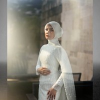 Gaun pengantin putih berlengan panjang itu memiliki siluet yang mengikuti bentuk tubuh. Gaun tersebut tampak simpel dan elegan dengan dipenuhi payet senada. Bagian lengannya dilengkapi kain menjuntai seperti cape yang jatuh sampai ke bawah, menciptakan kesan dramatis. Foto: Instagram/@deaaannisa