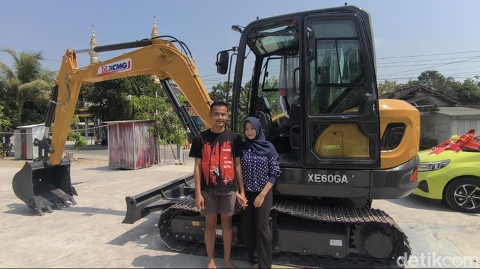 Pasangan asal Grobogan, Rico Putra Roberto Syah (23) dan Laella Nur Fadhilah (20) berfoto di depan ekskavator mahar pernikahan, Senin (10/8/2026).