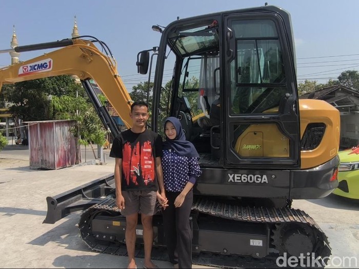 Pasangan asal Grobogan, Rico Putra Roberto Syah (23) dan Laella Nur Fadhilah (20) berfoto di depan ekskavator mahar pernikahan, Senin (10/8/2026).