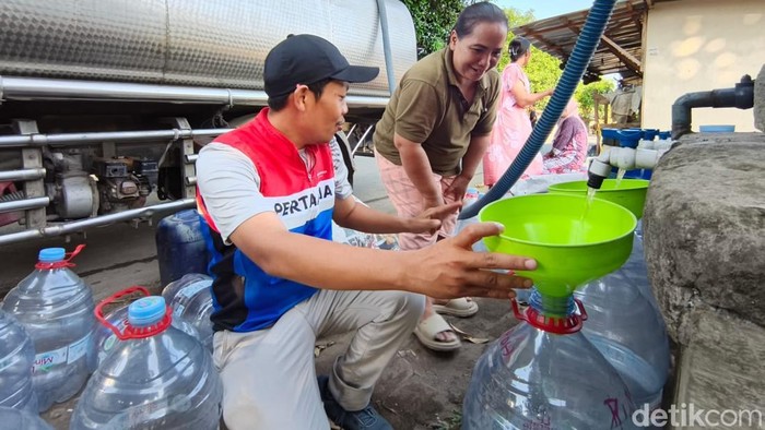Petugas dari Pertamina sedang membantu warga mengisi air bersih ke galon.