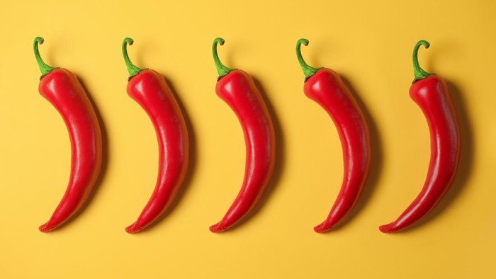 Five hot red peppers on a yellow background